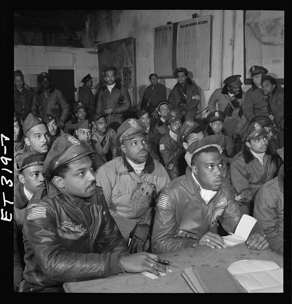 A group of military men watching a briefing and taking notes.